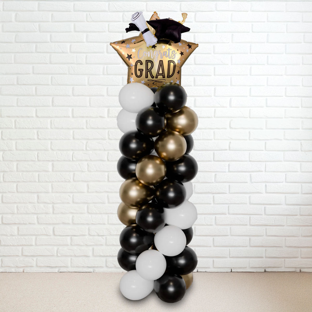 A tall balloon column with a graduation theme, featuring black, gold, and white balloons, topped with a 'GRAD' hat.