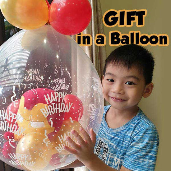 Boy holding up his gift in a balloon set, looking delighted and filled with joy.